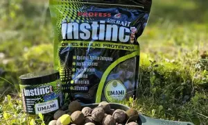 Czeskie kulki proteinowe Instinct Umami w zielonej łopatce, obok opakowania i słoiczka. Idealne na ryby!