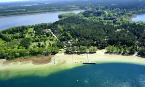 Malownicze jezioro Warchały otoczone lasem, z piaszczystą plażą, pomostami i kolorowymi łódkami.