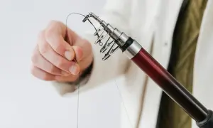 Dłoń przygotowuje żyłkę do wędkowania, pokazując, jak zrobic pętlę na końcu.