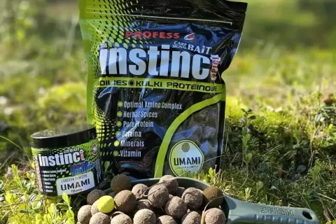Czeskie kulki proteinowe Instinct Umami w zielonej łopatce, obok opakowania i słoiczka. Idealne na ryby!