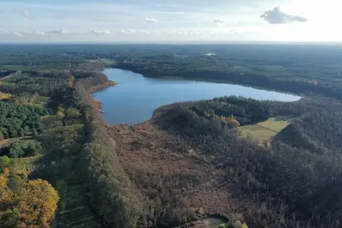 Malownicze jezioro wolickie otoczone lasami i polami. Spokojna tafla wody odbija błękitne niebo z chmurami.