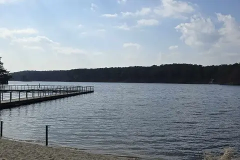 Drewniane molo na piaszczystym brzegu jeziora soczewka, otoczonego gęstym lasem.