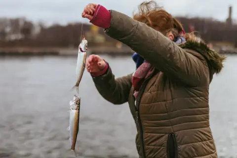 Udany połów na łowisku w Gdańsku – dwie ryby wiszą na żyłce, trzymanej przez kobietę w kurtce.