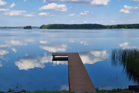 Drewniany pomost na spokojnym jeziorze przechlewskim, odbijającym błękitne niebo z białymi chmurami.