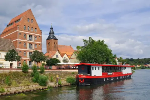 Statek "Hoffnung" cumuje przy brzegu rzeki Łaby w Niemczech, obok zabytkowych budynków i kościoła.
