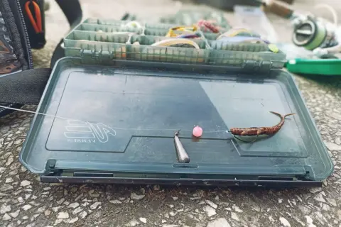 Gotowy jig rig na okonie: przynęta, różowa kulka i ciężarek na żyłce, leżą na otwartym pudełku wędkarskim.