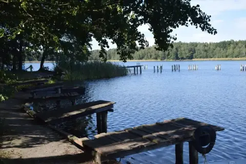Drewniane pomosty nad spokojnym, błękitnym jeziorem Chrzypsko Wielkie. W oddali widoczne paliki i zalesiony brzeg.