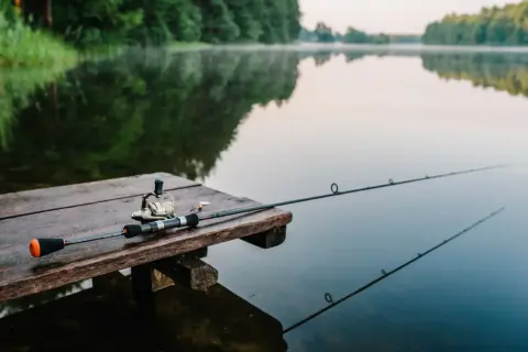 Wędka leży na drewnianym pomoście nad spokojnym jeziorem Tuchlin. Wczesny poranek, mgła unosi się nad wodą.