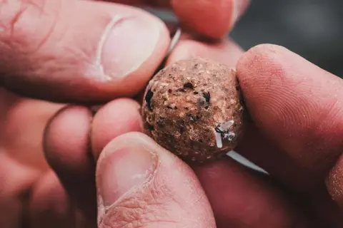 Dłoń trzyma kulkę zanętową z przyczepionymi gumkami do pelletu.