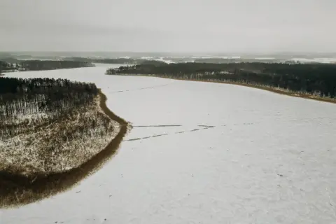 Zimowy krajobraz: zamarznięte jezioro Tyrkło otoczone lasem. Śnieg pokrywa taflę wody, tworząc białą, rozległą przestrzeń.