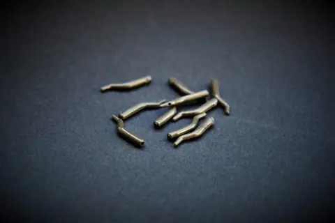 Metalowe pozycjonery haczyka, drobne akcesoria wędkarskie, leżą na ciemnym tle.