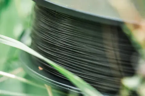Nawinięta na szpulę ciemna żyłka na spinning, otoczona zieloną trawą. Idealna do połowu drapieżników.