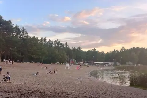 Plaża nad jeziorem w Jelczu-Laskowicach tętni życiem. Ludzie odpoczywają na piasku, kąpią się w wodzie, a dzieci bawią się przy dmuchanych zjeżdżalniach.