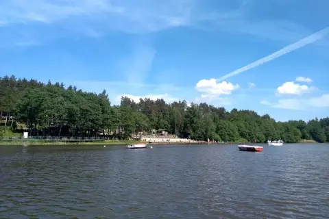 Spokojne jezioro Stobno otoczone zielonym lasem, z plażą i kilkoma łodziami.