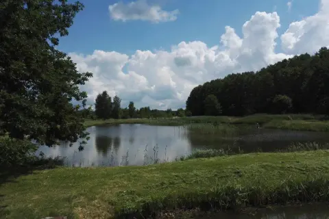 Spokojne łowisko Przemka nad jeziorem, otoczone zielenią i chmurami.