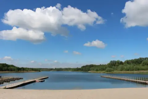 Piękny, słoneczny dzień nad jeziorem Wilczyńskim. Piaszczysta plaża, drewniane pomosty i błękitne niebo z białymi chmurami zapraszają do wypoczynku.