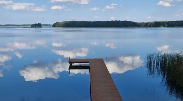 Drewniany pomost na spokojnym jeziorze przechlewskim, odbijającym błękitne niebo z białymi chmurami.