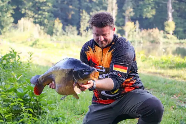 Wędkarz z dumą prezentuje okazałego karpia, który z pewnością nie jest ani sieją, ani sielawą.