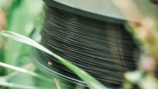 Nawinięta na szpulę ciemna żyłka na spinning, otoczona zieloną trawą. Idealna do połowu drapieżników.